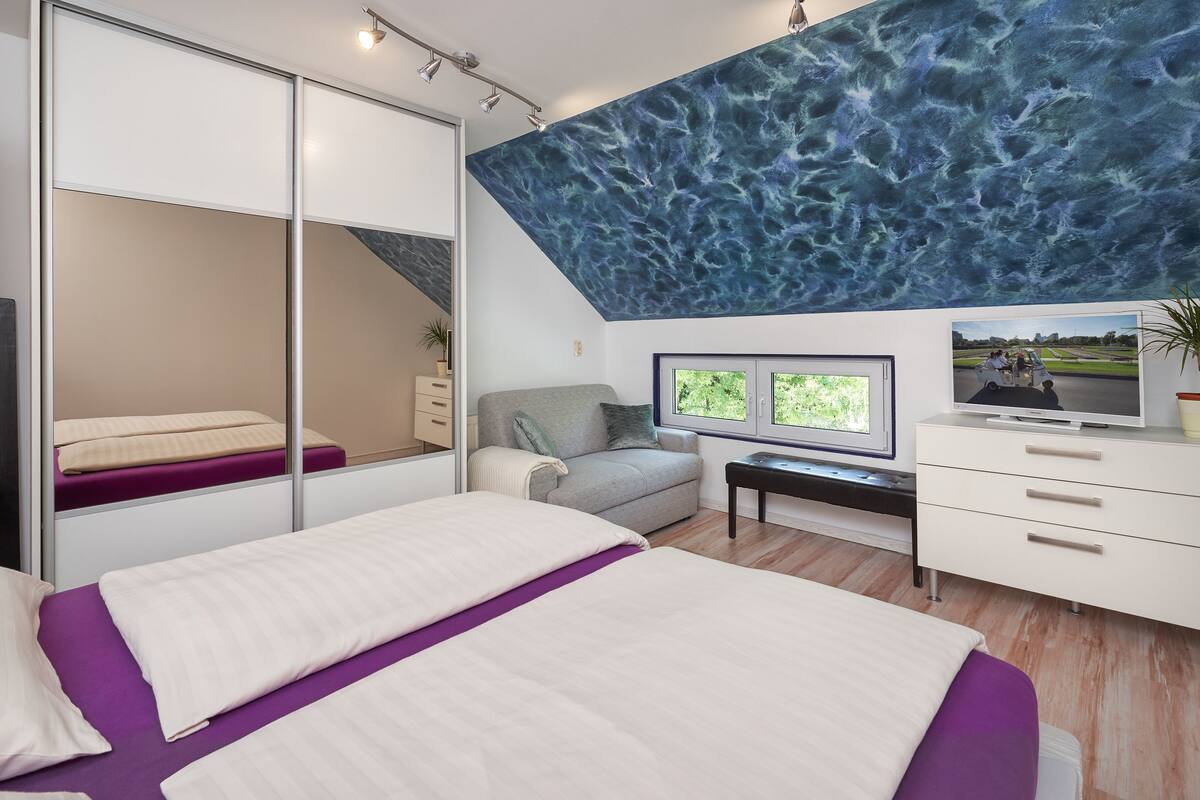 A modern bedroom with a large bed, a sofa, a desk, and a TV.