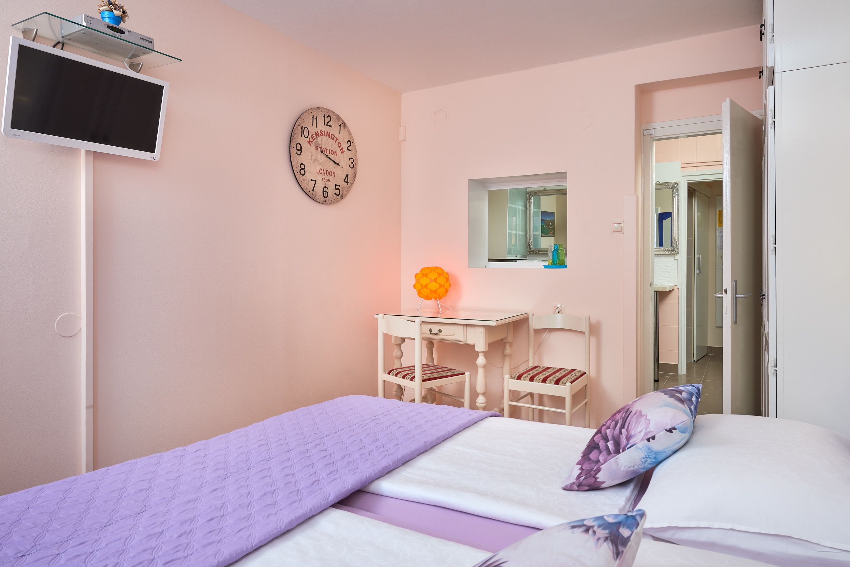 Een slaapkamer met een bed, een bureau, een stoel, een klok en een spiegel.