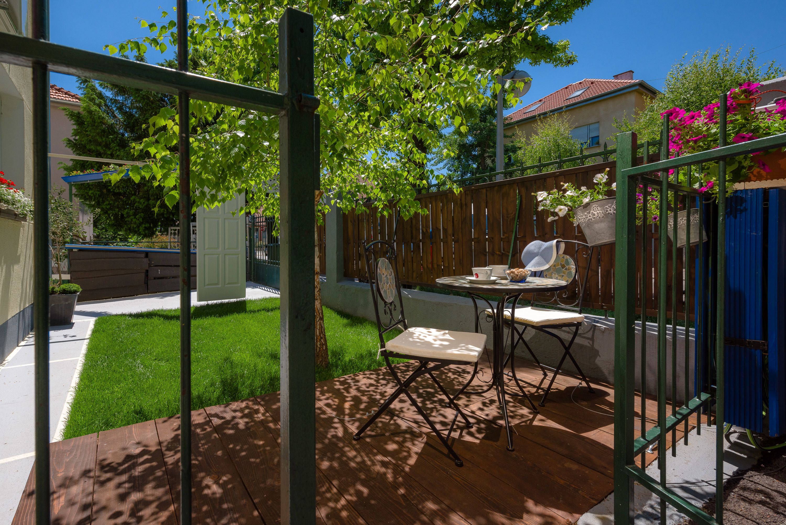 A patio with a table and chairs, surrounded by a wooden fence and a green metal gate.