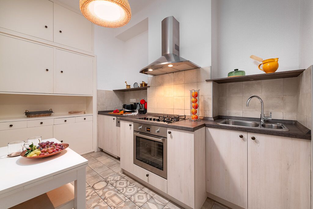 A modern kitchen with white cabinetry, a gas stove, a stainless steel range hood, and a sink.