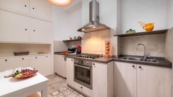 A modern kitchen with white cabinetry, a gas stove, a stainless steel range hood, and a sink.