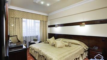 A hotel room with a large bed, a bedside table, a nightstand, a mirror, and a window with curtains.