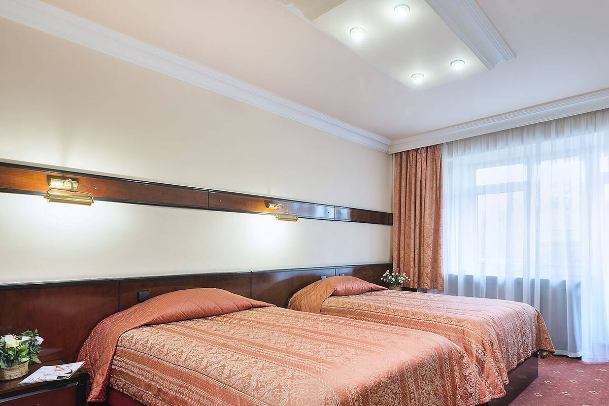 A hotel room with two beds, a desk with a television, and a window with curtains.