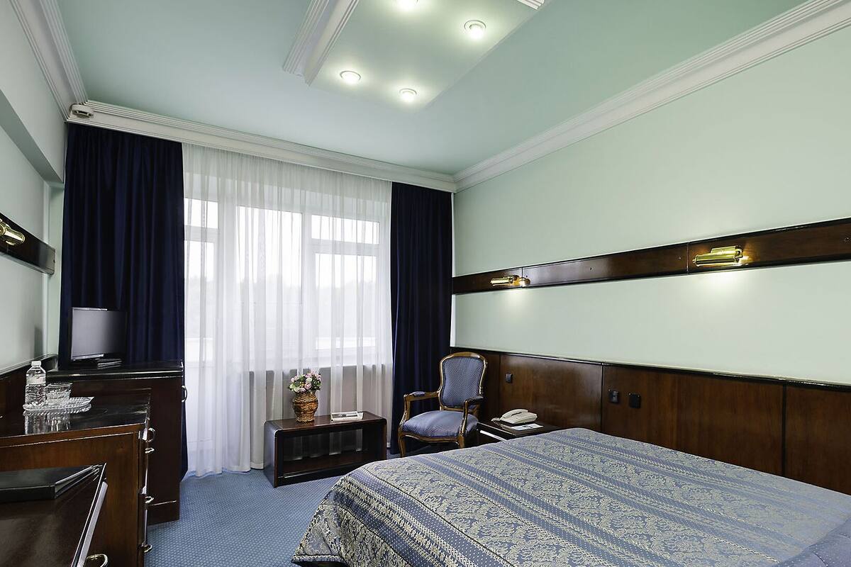 A hotel room with a bed, a desk, a chair, a television, and a window with curtains.
