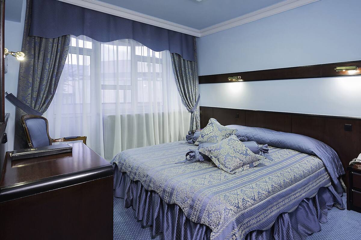 A bedroom with a large bed, a nightstand, a dresser, and a window with curtains.