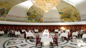 Une salle de banquet avec des tables rondes, des lustres somptueux et des fresques murales aux motifs élaborés.