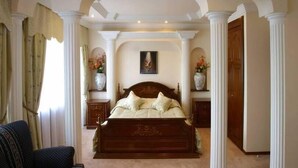 Une chambre à coucher avec un grand lit, deux tables de chevet, un tableau au mur et une porte sur le côté droit.