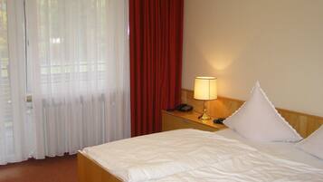 A hotel room with a bed, a nightstand with a lamp, a telephone, and a window with curtains.