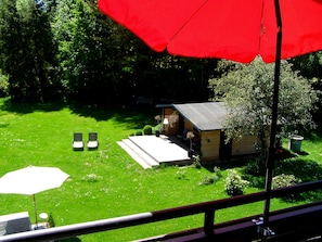 Een klein houten huisje met een veranda, omringd door een gazon en bomen.
