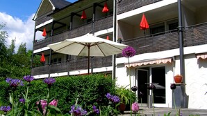 A multi-story building with balconies, outdoor umbrellas, and potted plants. - Haus Katharina - Hotel am Park (Bad Steben)