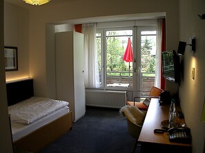 Hotelkamer met een bed, bureau met telefoon, stoel, raam met gordijnen en een radiator.
