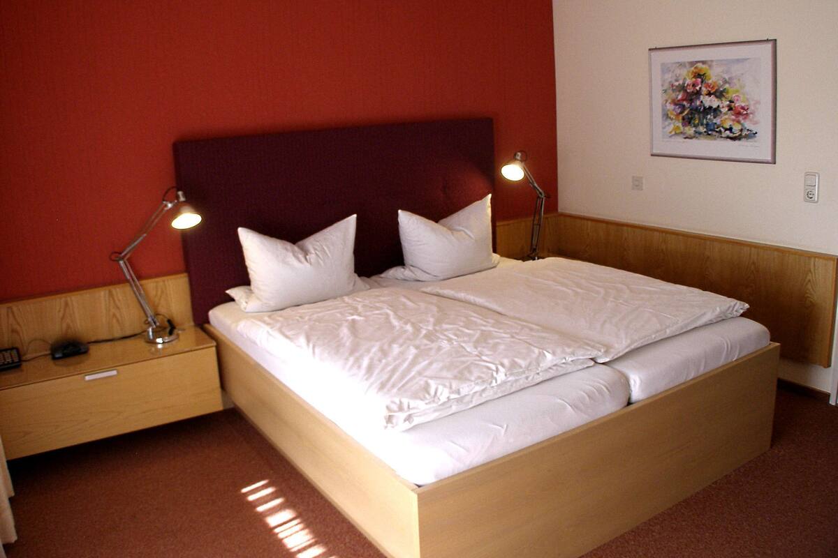 A neatly made bed with white linens, two bedside lamps, and a wooden headboard.