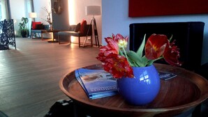 A living room with a wooden coffee table holding a blue vase with red flowers, a magazine, and a remote control. - Haus Katharina - Hotel am Park (Bad Steben)