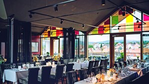 A restaurant with multiple tables set for dining, large windows offering a view of the city, and a modern interior design.