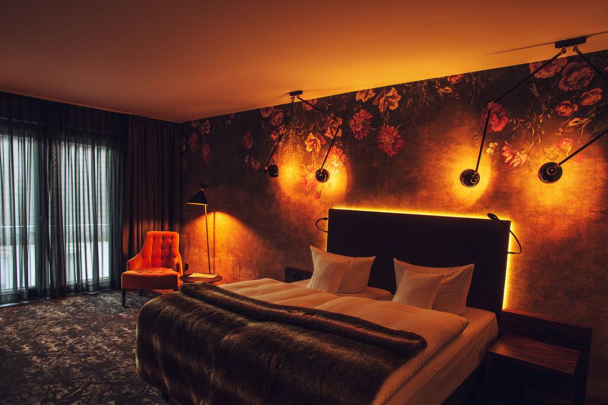 Une chambre d’hôtel avec un grand lit, une chaise, une table de chevet et un mur recouvert d’un papier peint à motifs floraux.