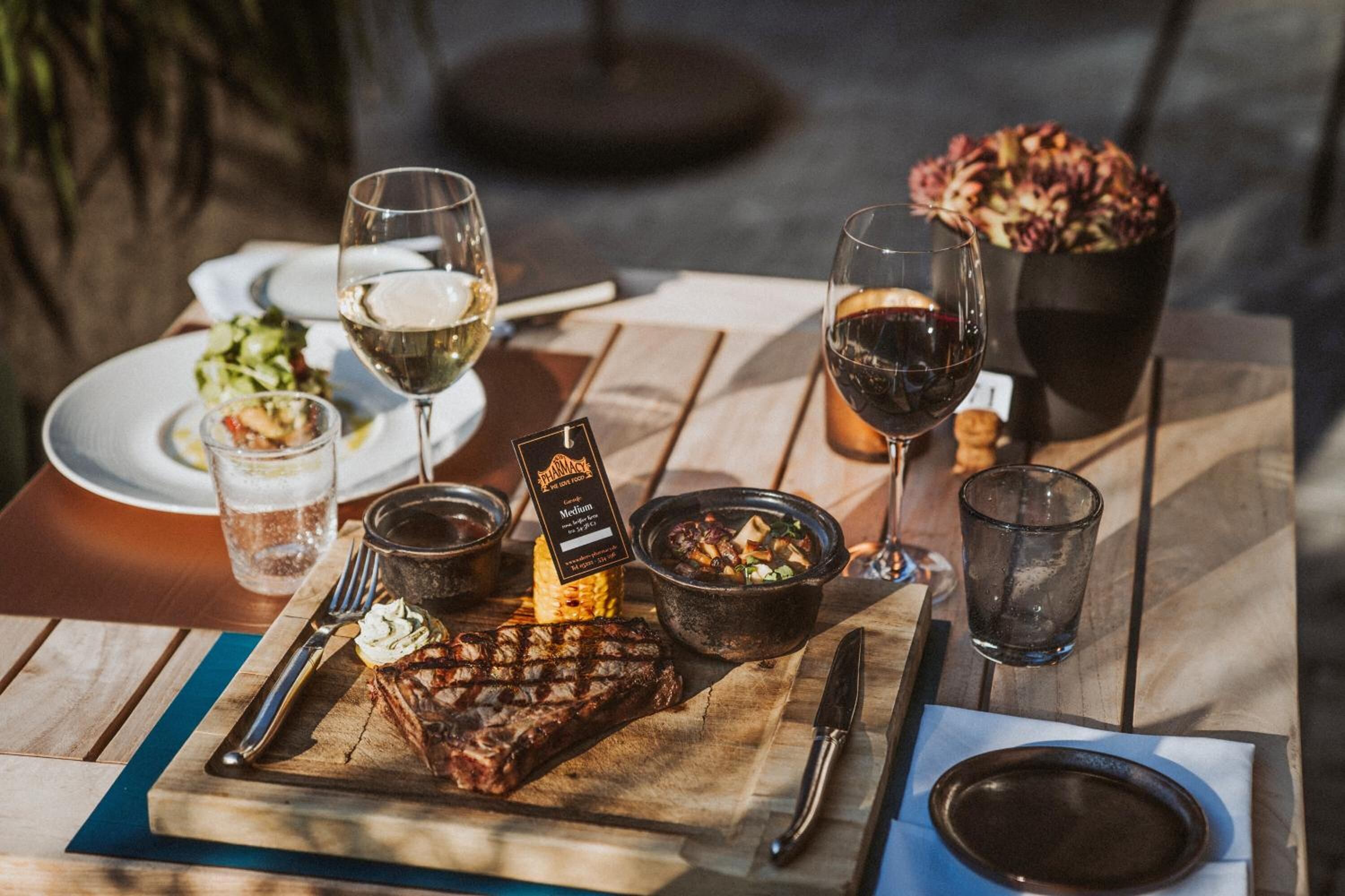 A wooden table with a grilled steak, a bowl of salad, and two glasses of wine.