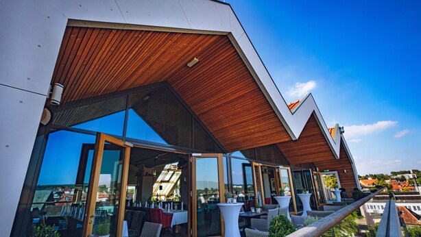 A modern outdoor seating area with glass doors, wicker furniture, and a wooden ceiling.