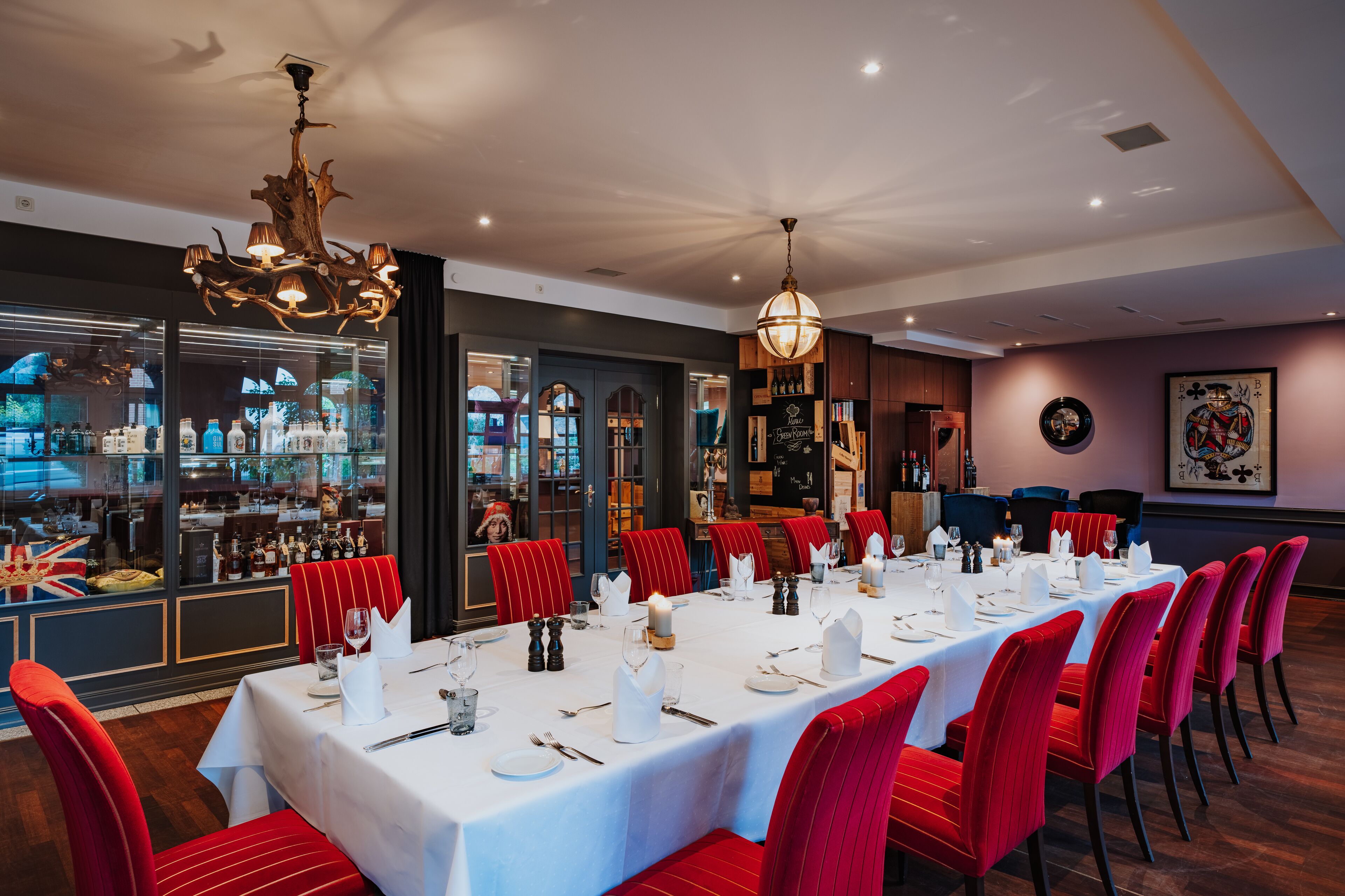 A formal dining room with a long table set for a meal, red upholstered chairs, and a chandelier.
