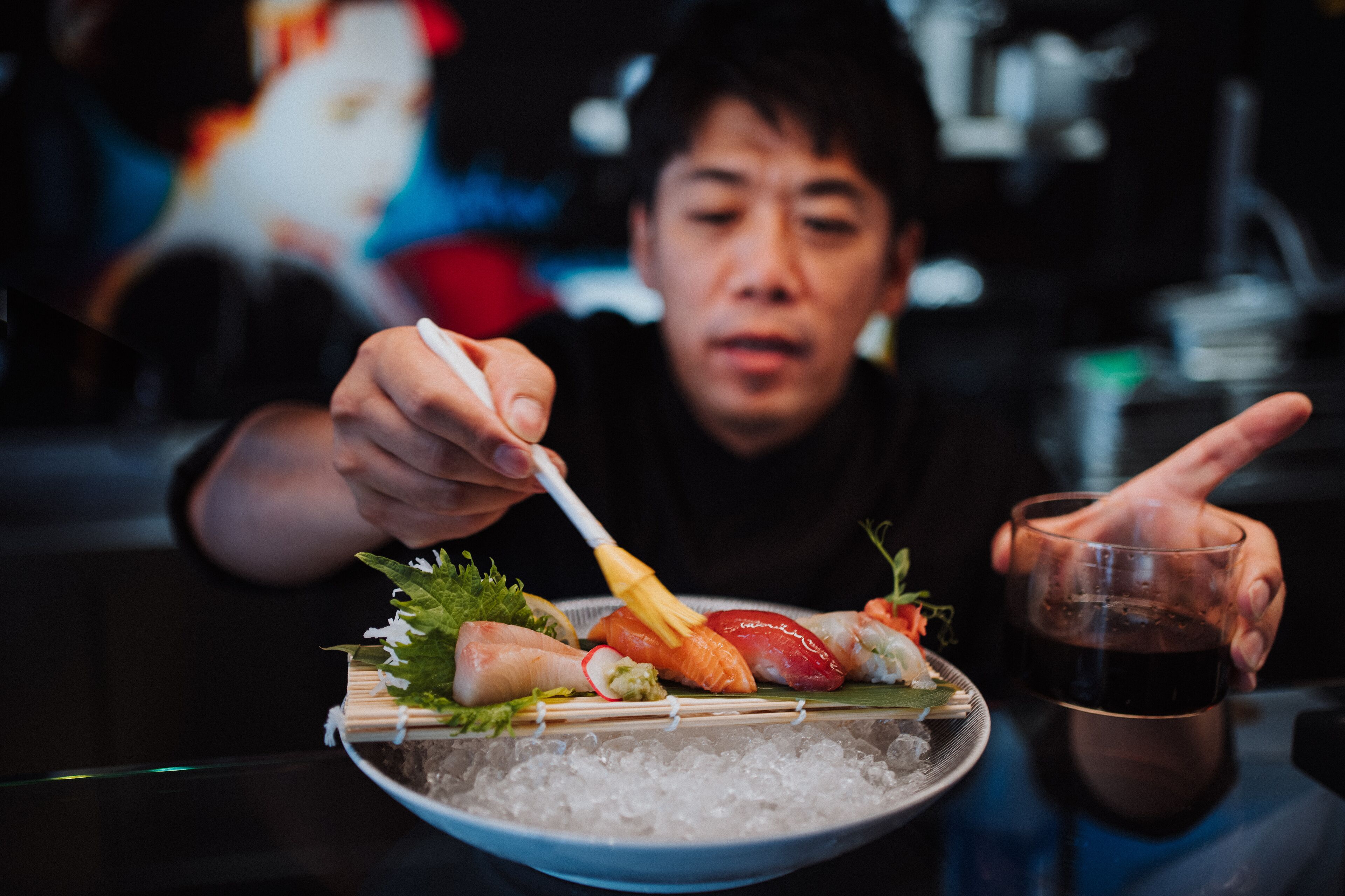 A person eating sushi with chopsticks and holding a glass of drink.
