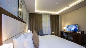 A hotel room with a large bed, a desk with a television, and a chair. - The Town Hotel Doha (Doha)