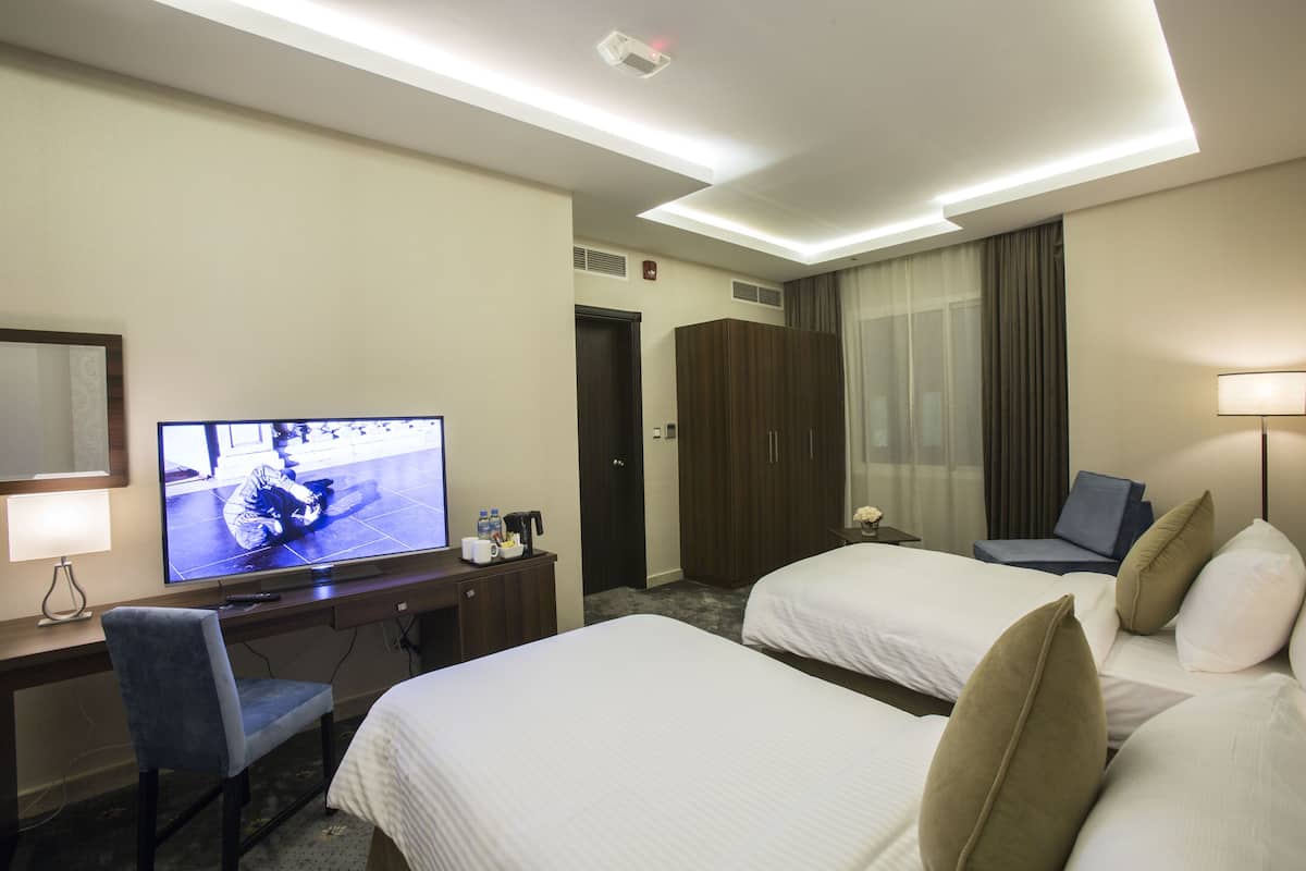 A hotel room with two beds, a desk with a TV, a chair, a wardrobe, and a lamp.