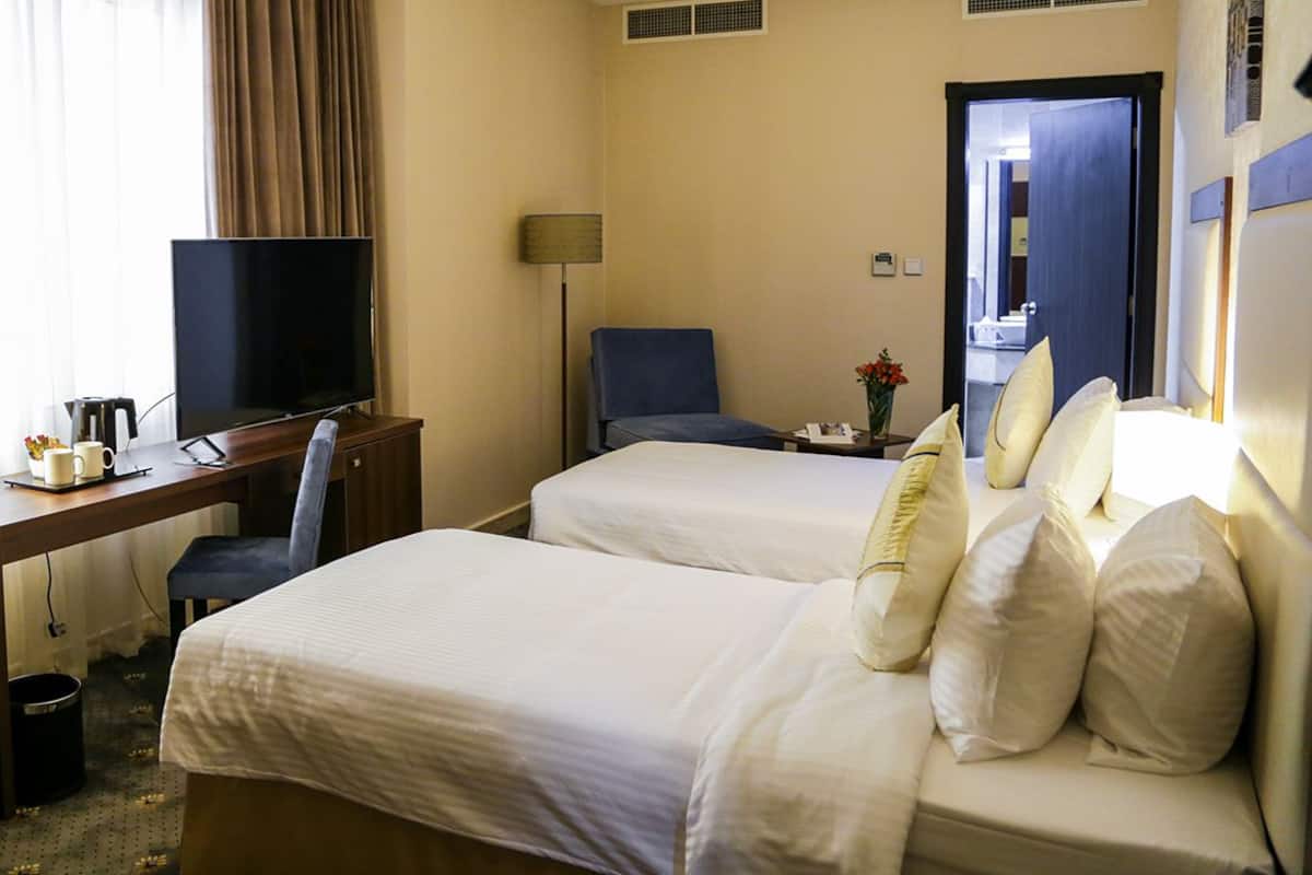 A hotel room with two beds, a desk with a TV, a chair, and a lamp.