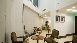 A spacious lobby with high ceilings, a marble floor, and classic furniture. There are framed pictures on the wall and a potted plant in the center. - The Town Hotel Doha (Doha)