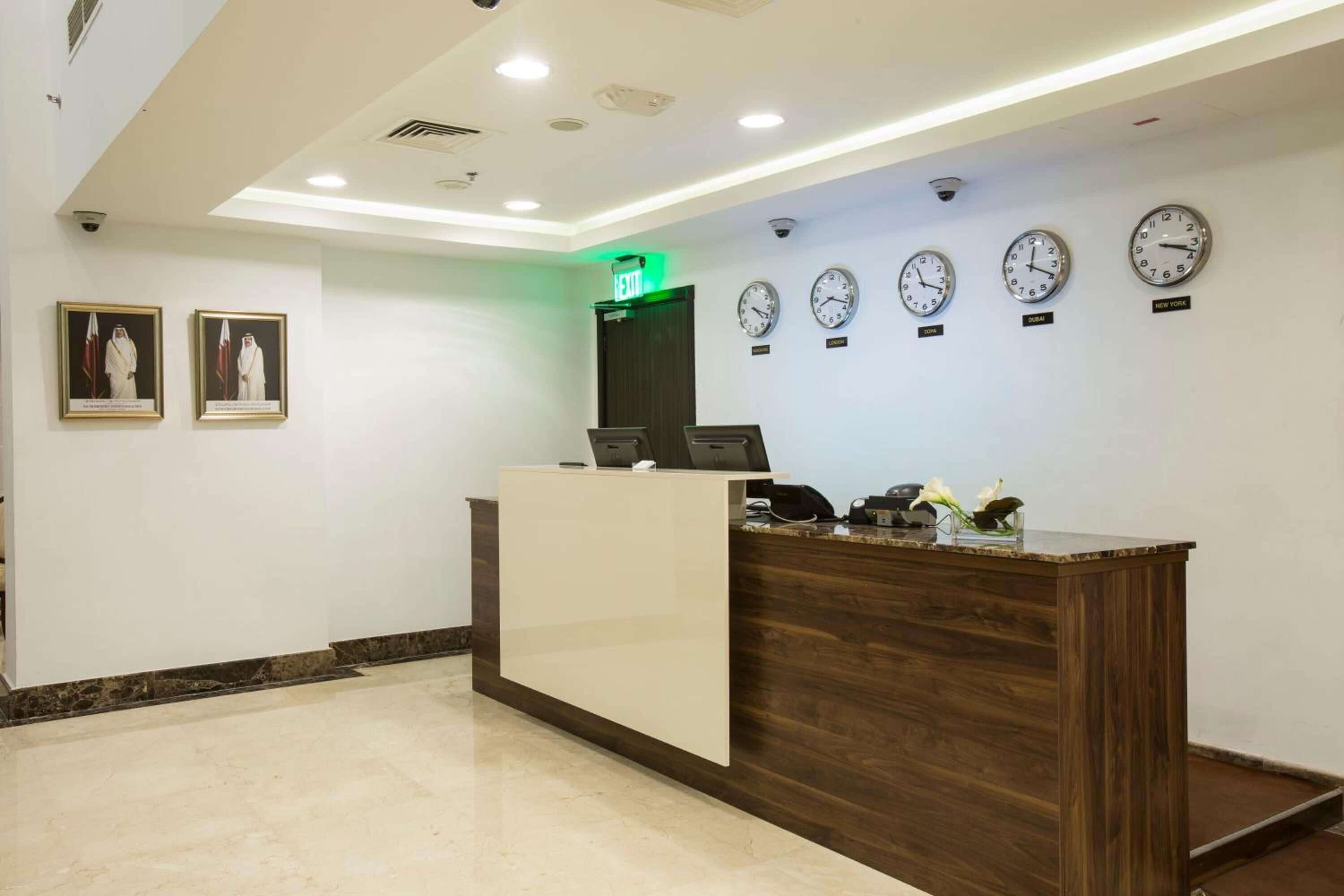 A reception desk with clocks displaying different time zones, framed pictures on the wall, and a green exit sign.