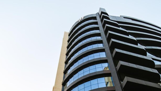 A modern building with a curved facade and multiple flags displayed outside. - The Town Hotel Doha (Doha)