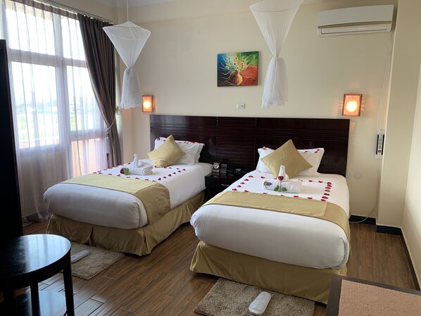 A hotel room with two beds, each with a canopy, a painting on the wall, and an air conditioning unit. - Delano Hotel (Bahir Dar)
