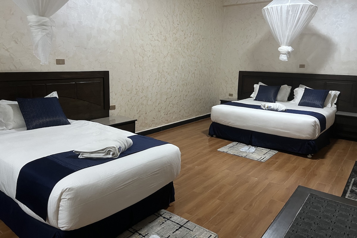 A hotel room with two beds, wooden flooring, and a canopy bed.