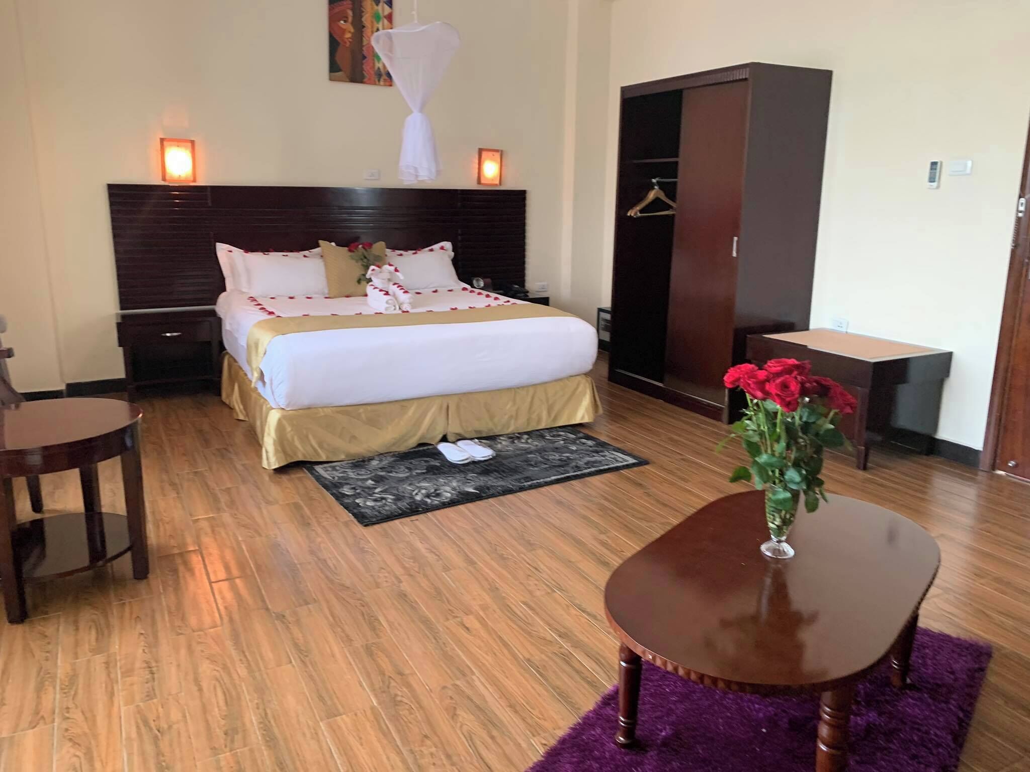 Ein Hotelzimmer mit Bett, Nachttischen, einem Schreibtisch, einem Kleiderschrank und einem kleinen Tisch mit Blumenvase.