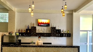 A bar area with a marble countertop, three bar stools, a TV mounted on the wall, and shelves with bottles and glasses. - Delano Hotel (Bahir Dar)