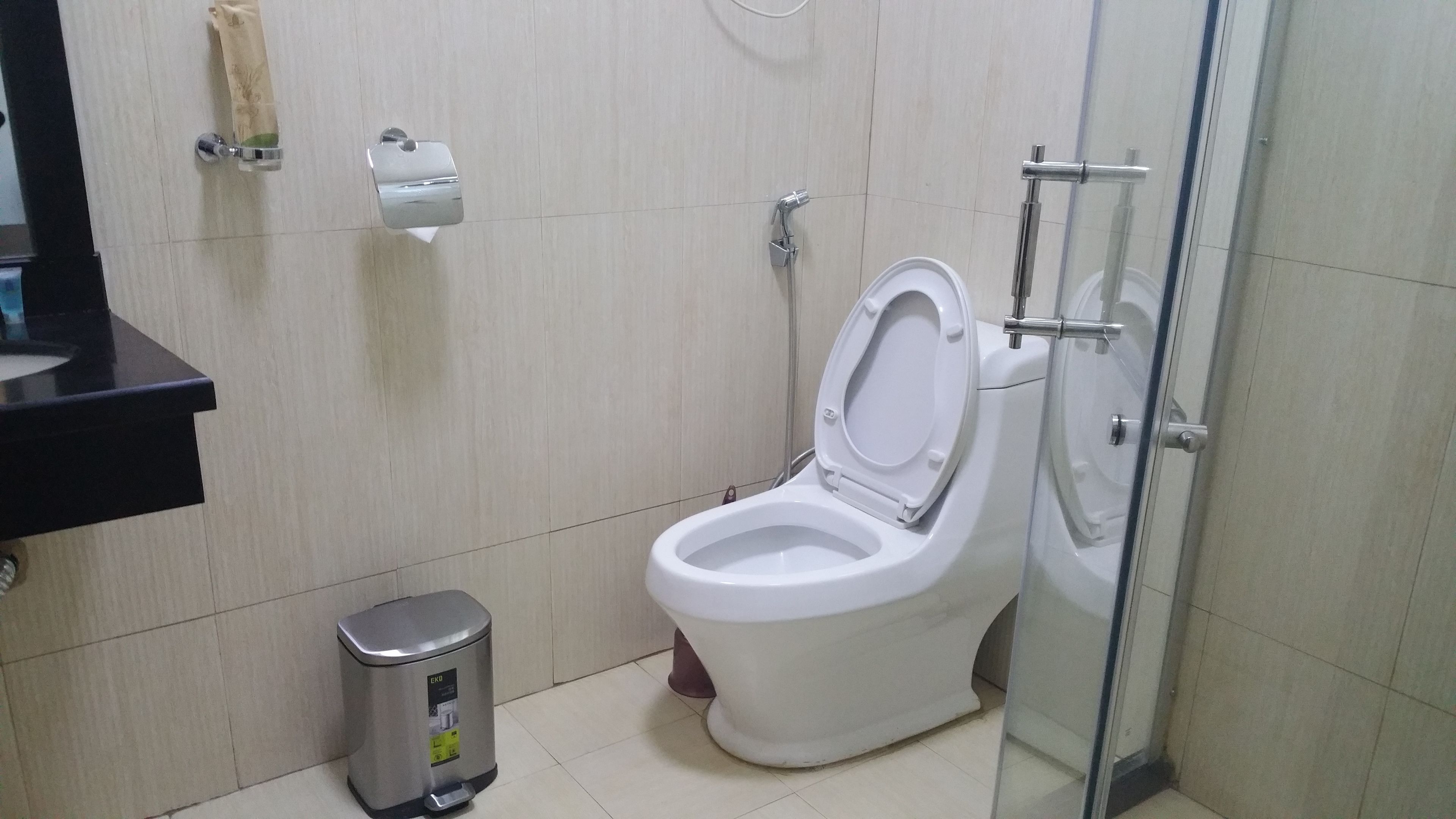 Une salle de bain avec des toilettes blanches, une poubelle et une cabine de douche en verre.
