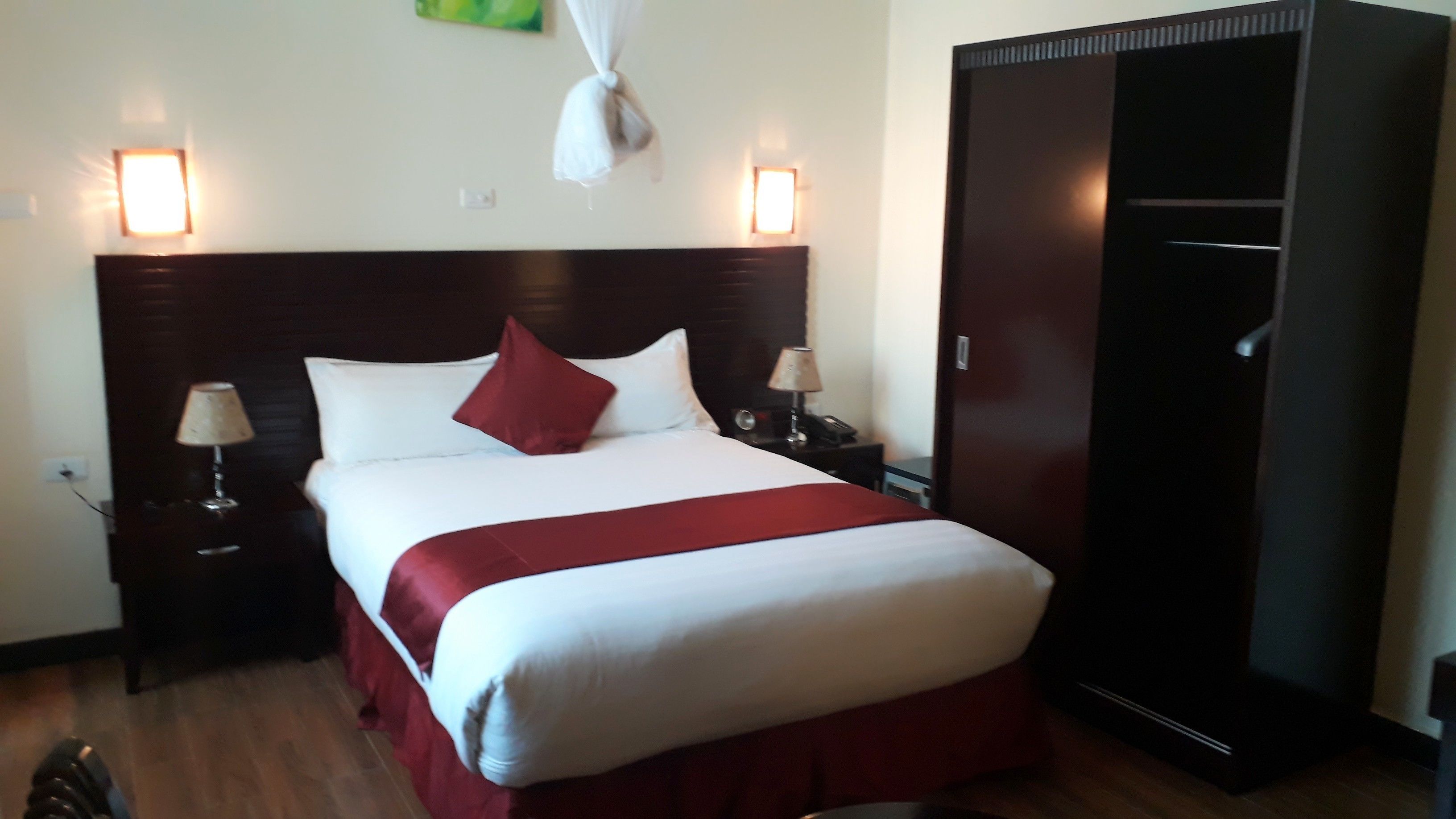 A neatly made bed with a red and white bedspread, two bedside lamps, and a dark wooden wardrobe.