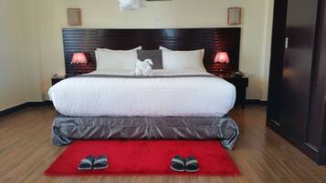 A neatly made bed with a red rug and slippers in front, wooden headboard, two bedside lamps, and a framed picture on the wall.