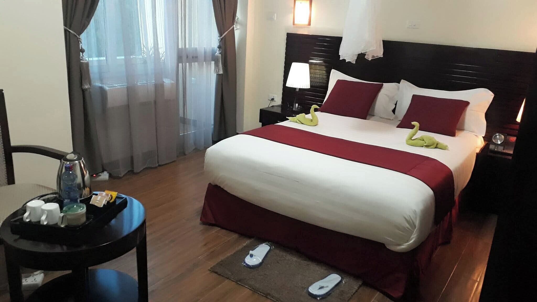 Ein Hotelzimmer mit einem Bett, einem Nachttisch, einer Lampe, einer Kaffeemaschine und einem Tisch mit Flasche und Gläsern.