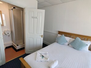 Une chambre d’hôtel avec un lit, des oreillers, une serviette, une tête de lit en bois, une porte blanche et un espace douche.