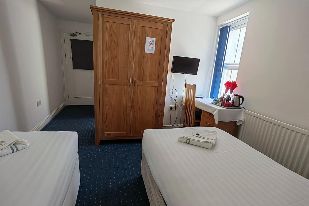 A hotel room with two beds, a wardrobe, a desk with a computer, and a window with curtains.