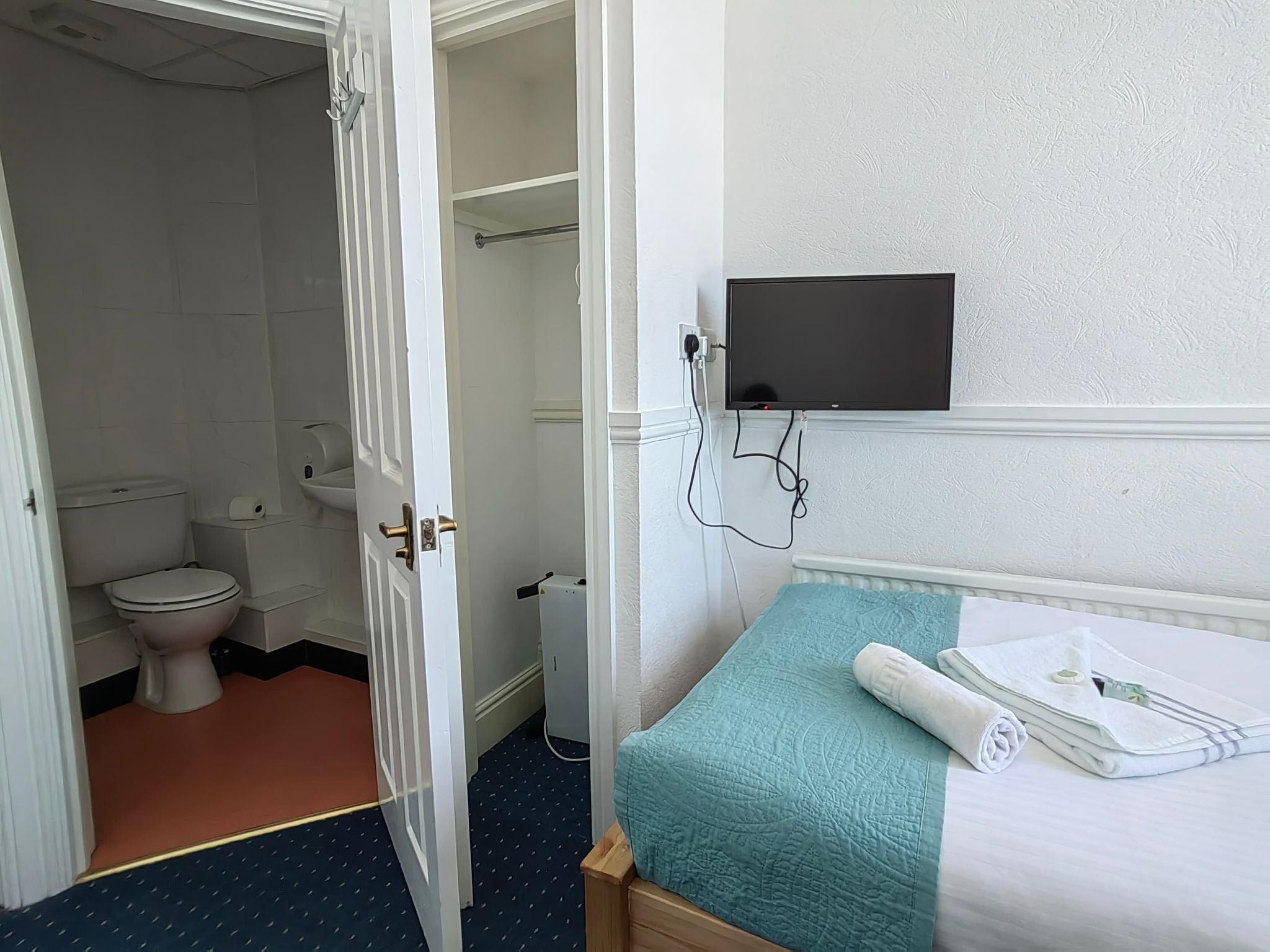 A hotel room with a bed, a television mounted on the wall, a bathroom with a toilet and sink, and a door leading to another room.