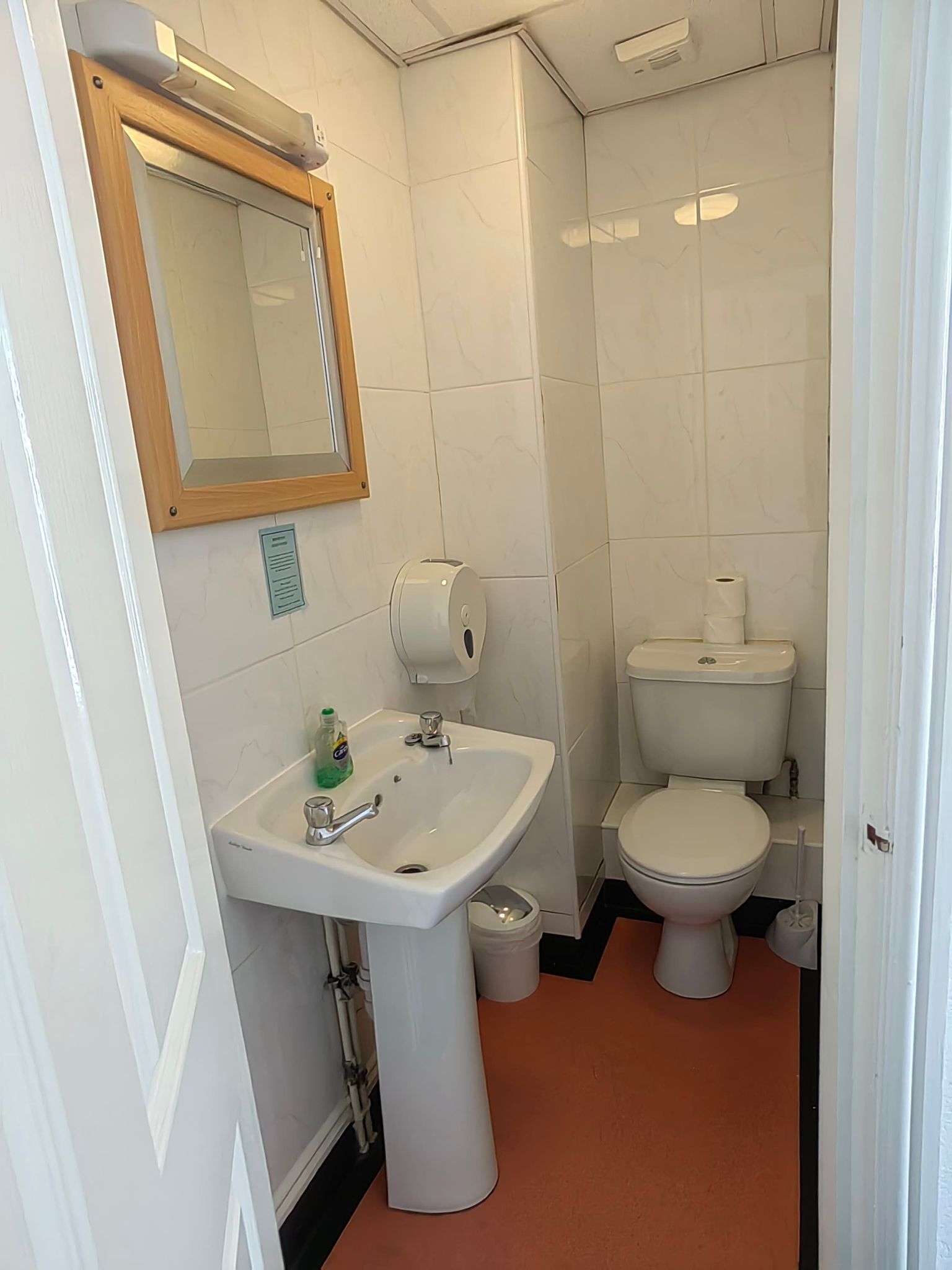 Une salle de bain avec un lavabo blanc, un miroir, des toilettes et une poubelle.
