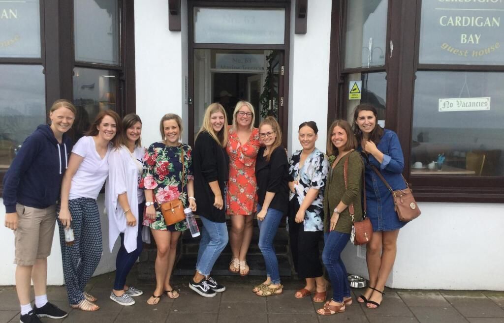 Un grupo de personas frente a un edificio con un letrero que dice 'CARDIGAN BAY guest house'.