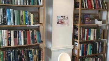 A library with bookshelves filled with books, a white chair, and a sign indicating all books are £5 each.