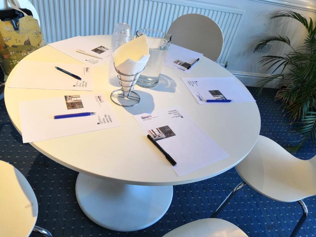 A round table with documents, pens, and a glass of water.