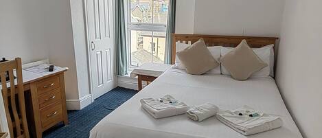 Una habitación de hotel con una cama, un escritorio de madera, una silla y una ventana con cortinas.