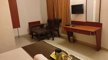 A hotel room with a bed, a desk, a chair, a TV, and a tray with a cup and a thermos.