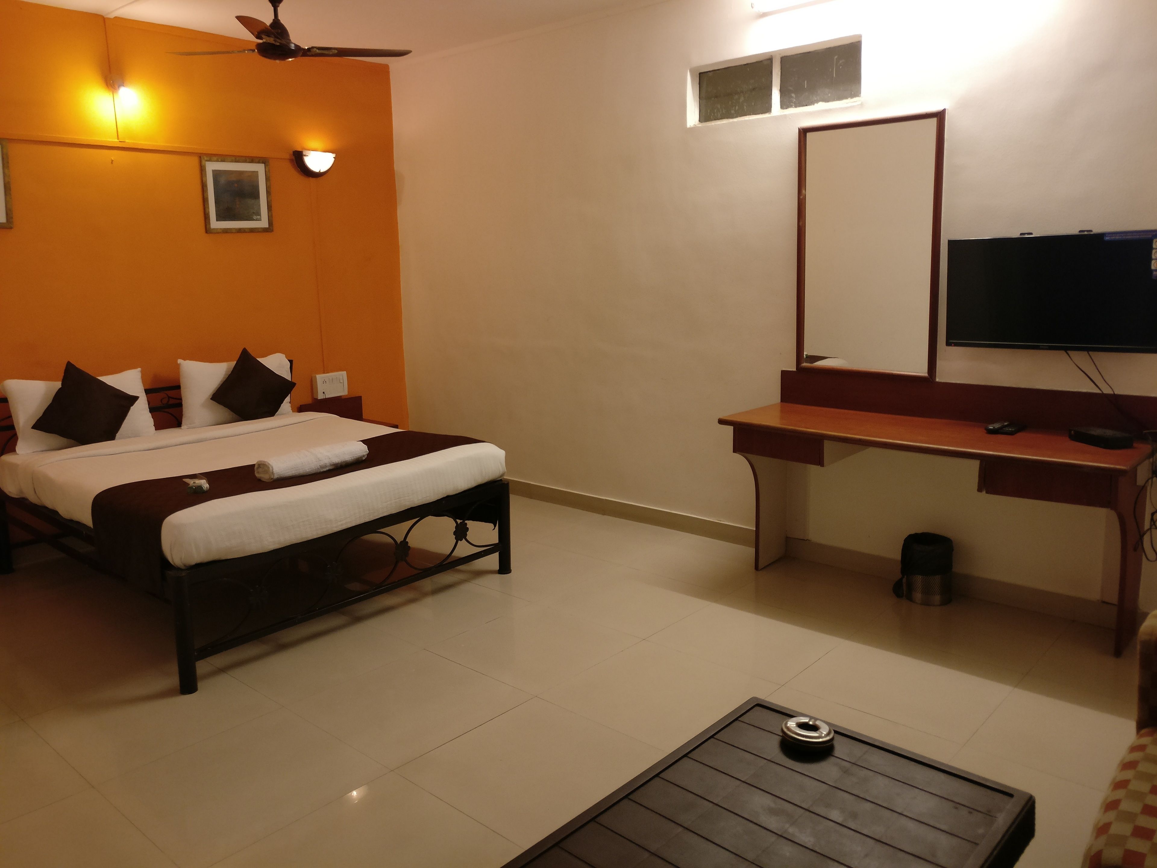 Quarto de hotel com cama, escrivaninha, televisão e ventoinha no teto.