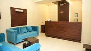 A reception area with a blue sofa, a wooden reception desk, and a ceiling fan. - HMR Royal Inn (Pune)