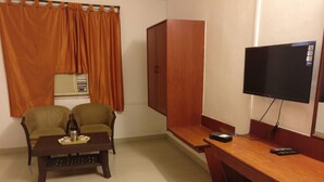 A compact room with a wooden desk, two armchairs, a television, and a small trash bin. - HMR Royal Inn (Pune)