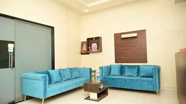 A room with two blue sofas, a small wooden coffee table, and a cabinet with framed pictures. - HMR Royal Inn (Pune)